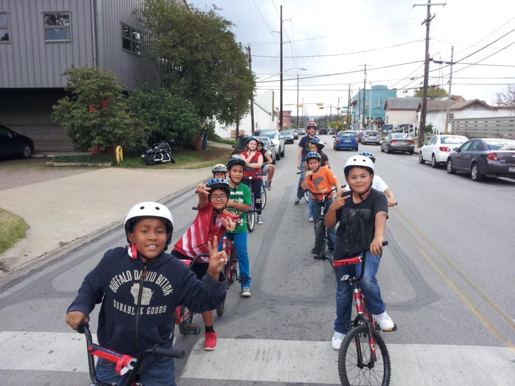 Two lines of elementary school students on bikes waiting at a stoplight.