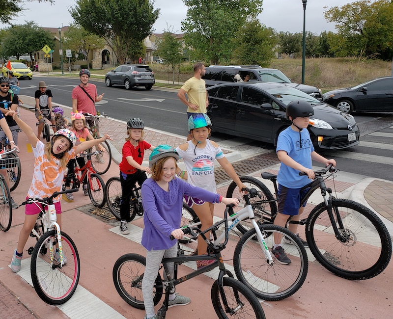 Large group of elementary school aged cyclists in a protected bike lane.