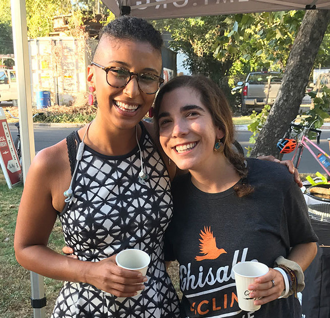 Two smiling women at a Bike to Work Day fueling station with coffee cups.