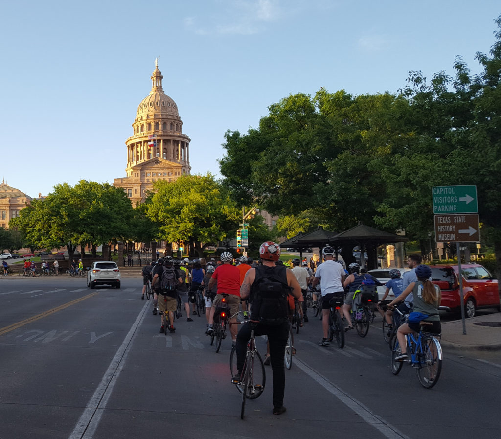 Large group of cyclists riding towards the Texas State Capitol.
