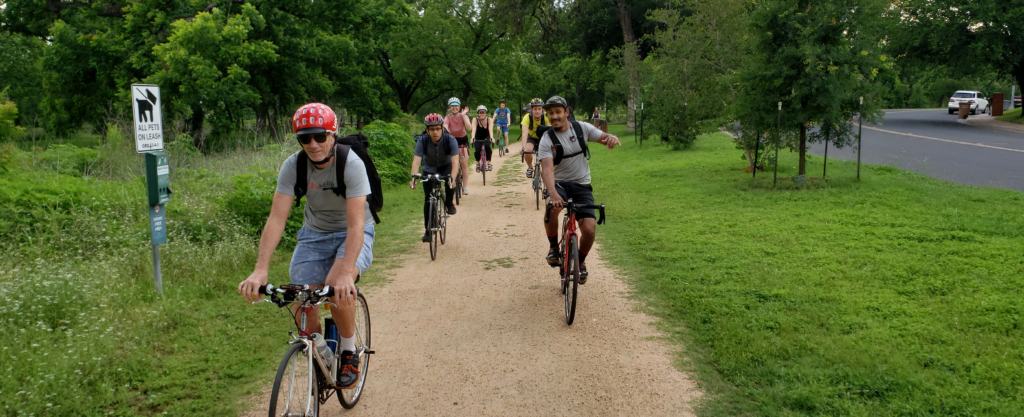 Group of cyclists casually riding on trail in a park.